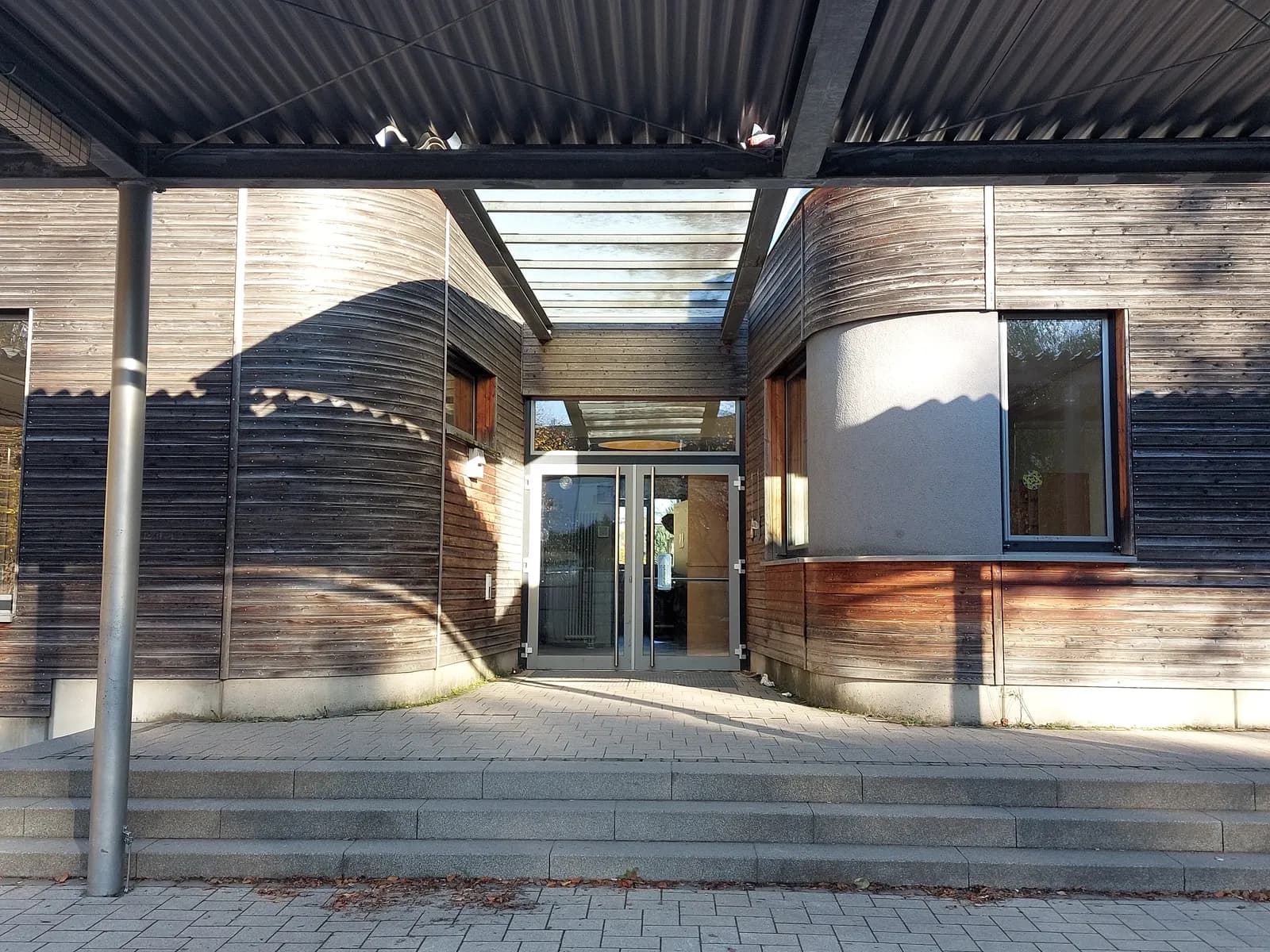 Geschwungene Holzarchitektur am Eingang der Regenbogenschule